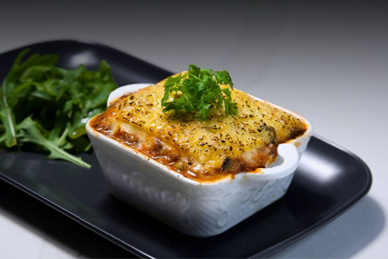 Savor lasagna with a golden, blistered cheese top, served with rocket